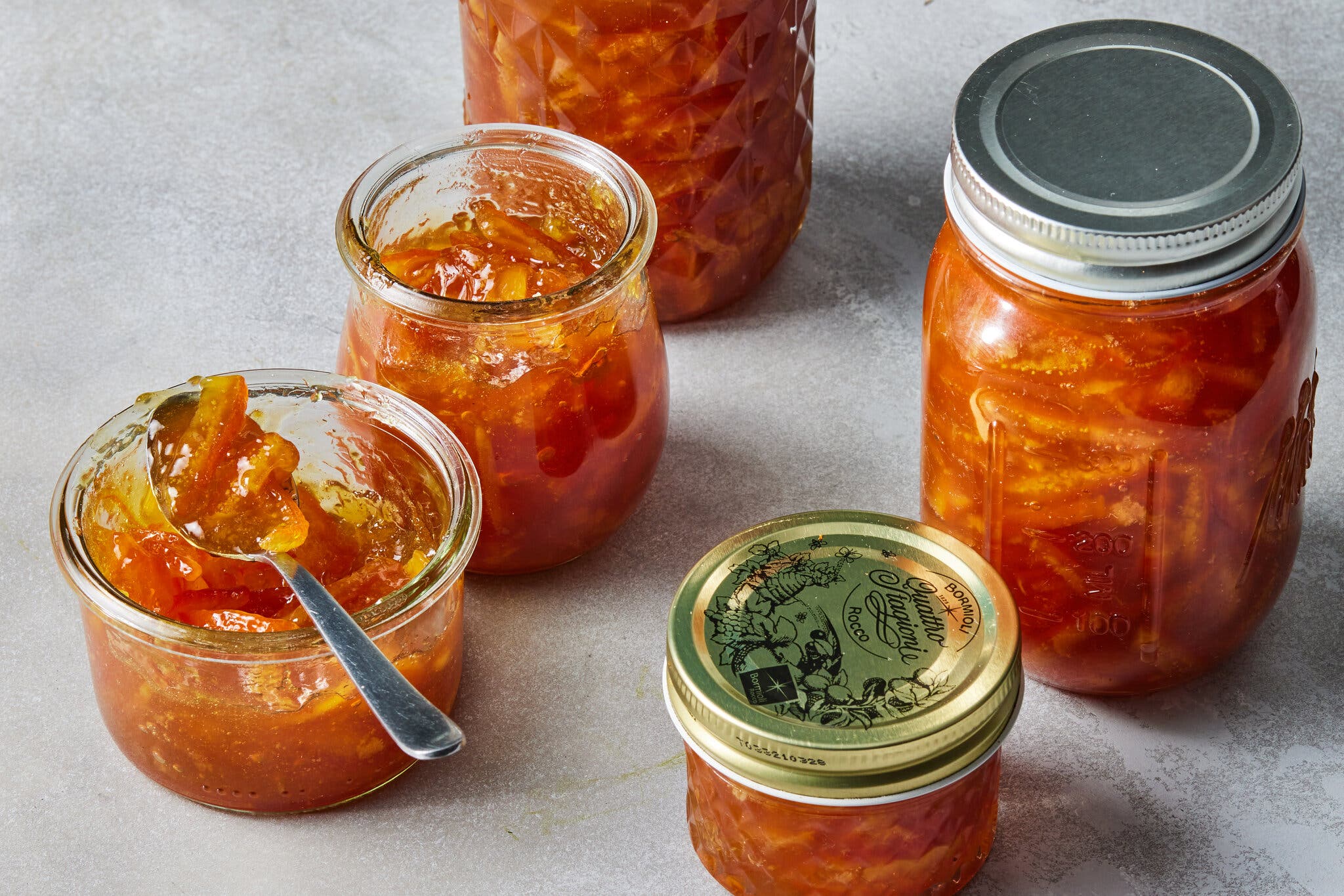 Five jars of marmalade, one open with a spoon inside.