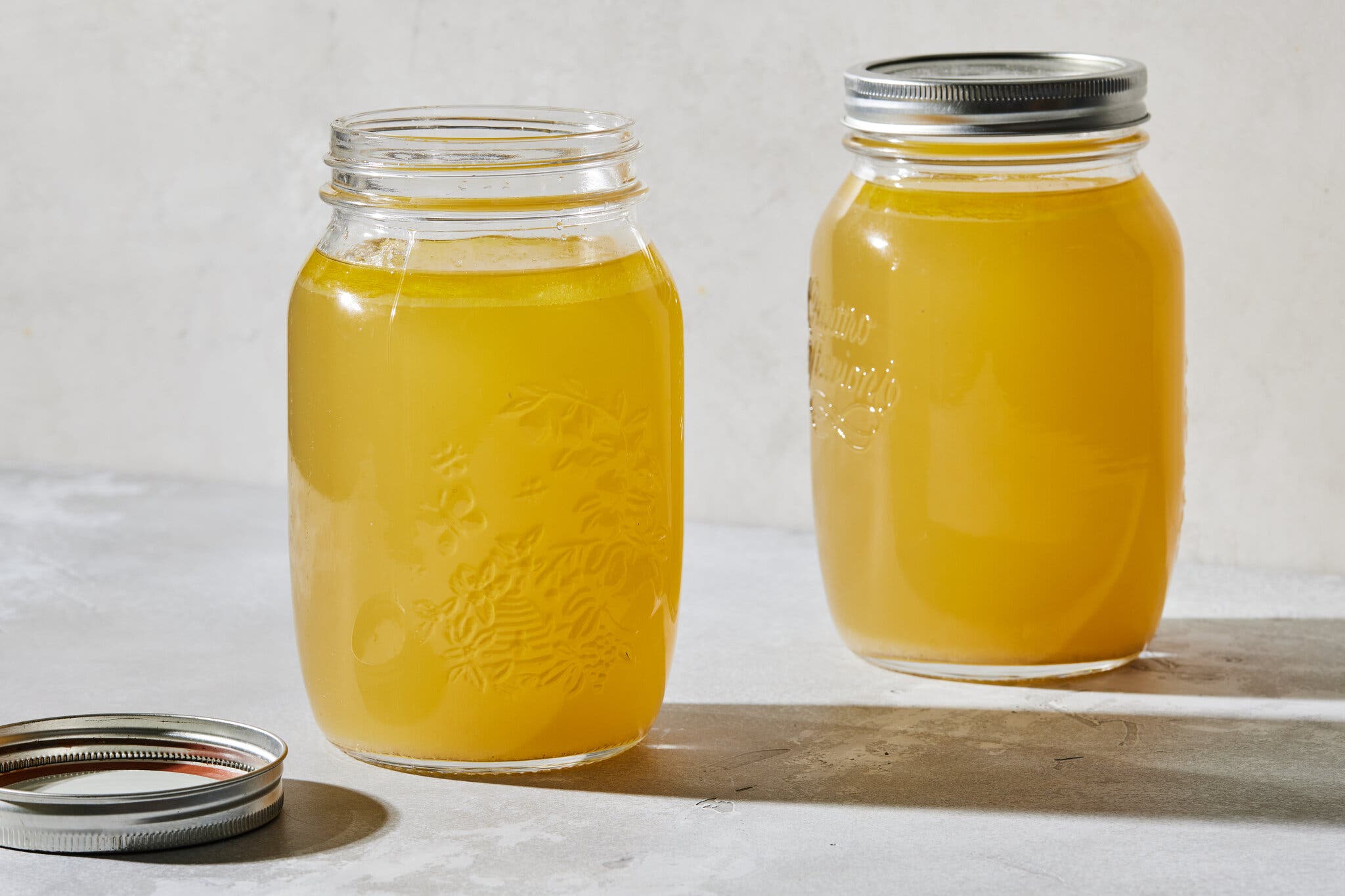 Two Mason jars of golden liquid rest on a counter.