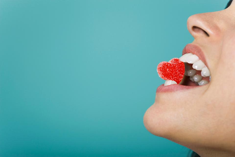 Person biting a heart-shaped gummy with teeth visible against a blue background