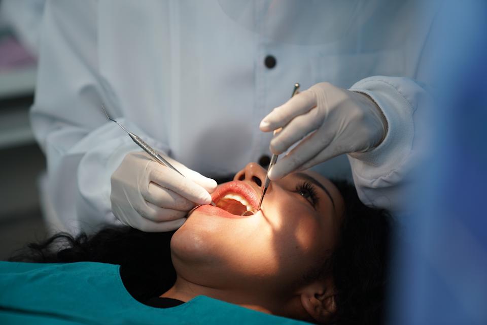 Person lying in a dental chair receiving a dental examination by a professional wearing gloves and a white coat