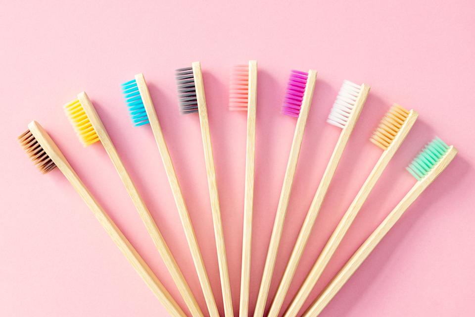 Bamboo toothbrushes with multicolored bristles are fanned out on a plain background