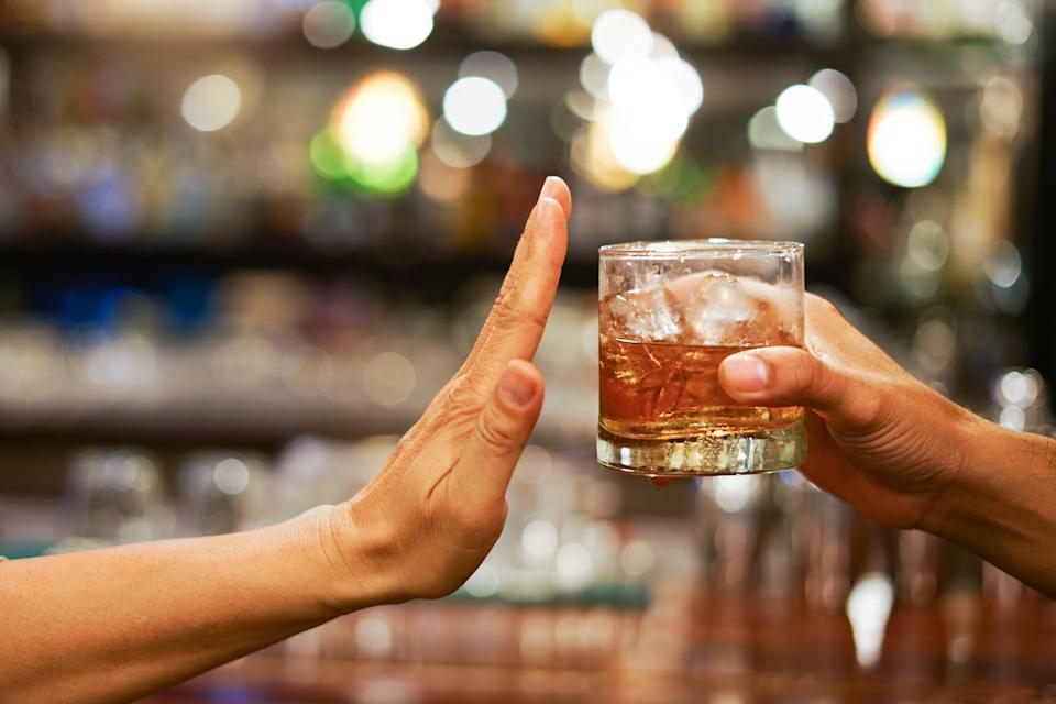 A hand gestures "stop" as another offers a glass of whiskey with ice, suggesting refusal or abstaining from alcohol