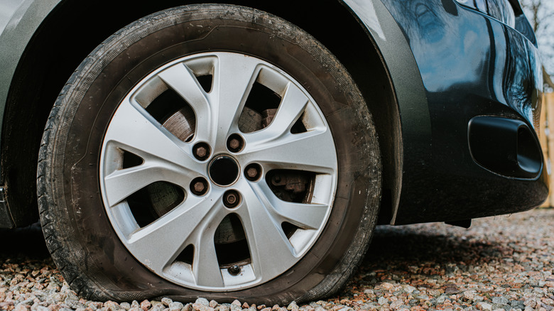 a close up image of a flat car tire parked on gravel