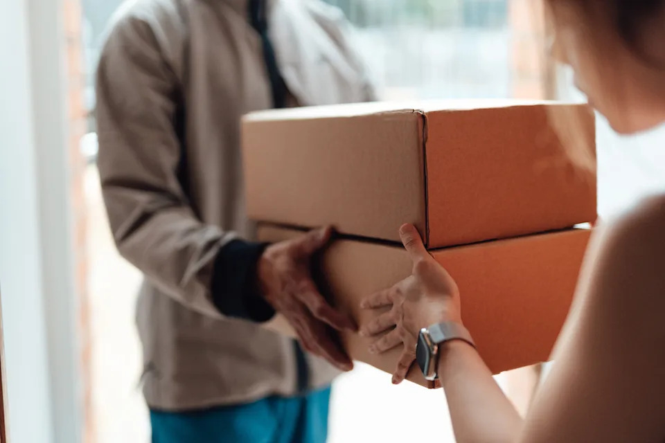 Person handing two cardboard boxes to another person, depicting a delivery or package exchange scenario