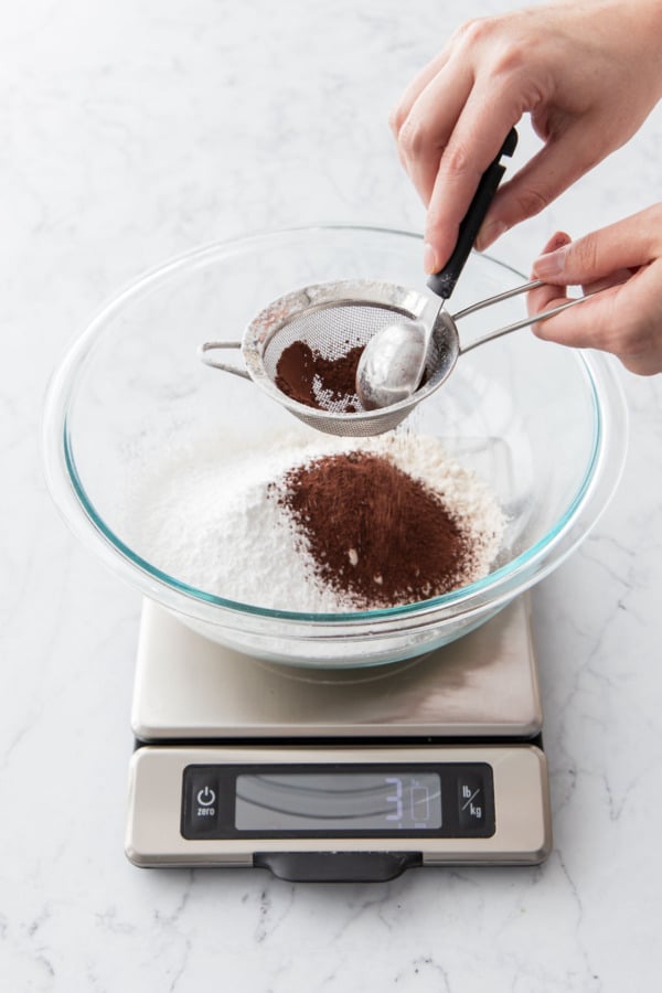 Sifting cocoa powder into a mixing bowl along with flour, salt, and powdered sugar.