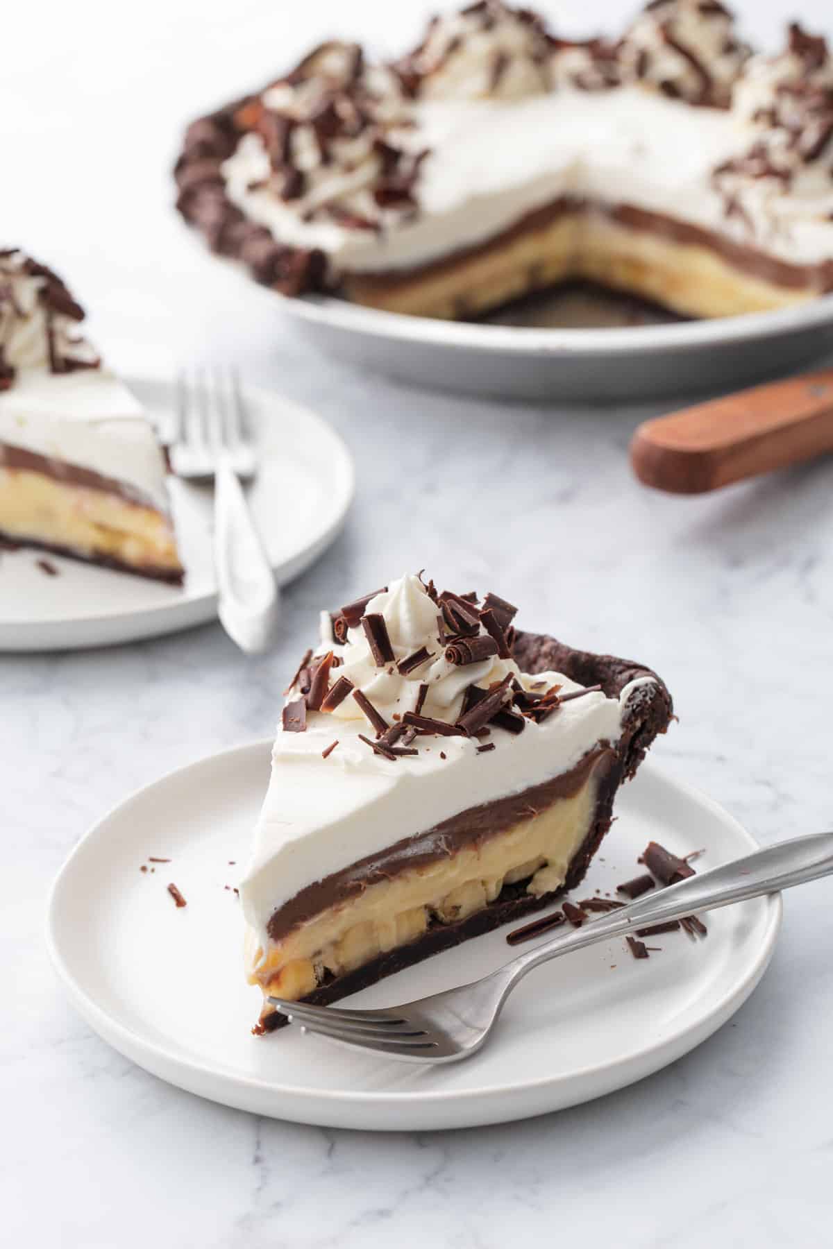 Chocolate Banana Cream Pie with Flaky Chocolate Pie Crust sliced on white plates on marble background.