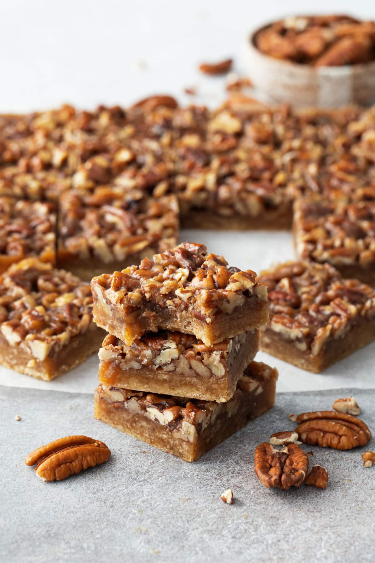 Stack of Pecan Pie Shortbread Cookie Bars, one with a bite taken out of it to show the texture and layers.