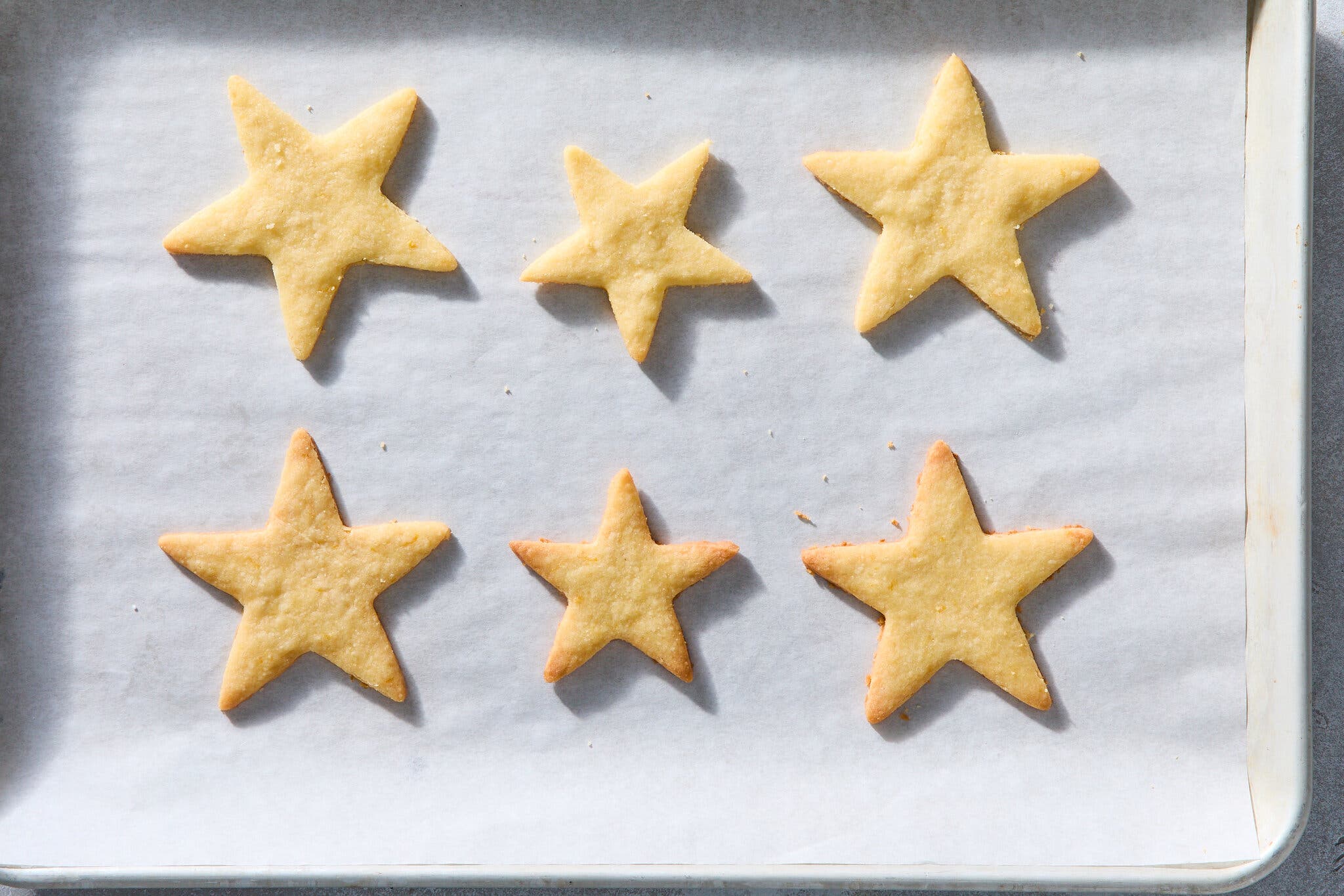 An overhead image of six star cookies on a piece of parchment paper set into a rimmed baking sheet.