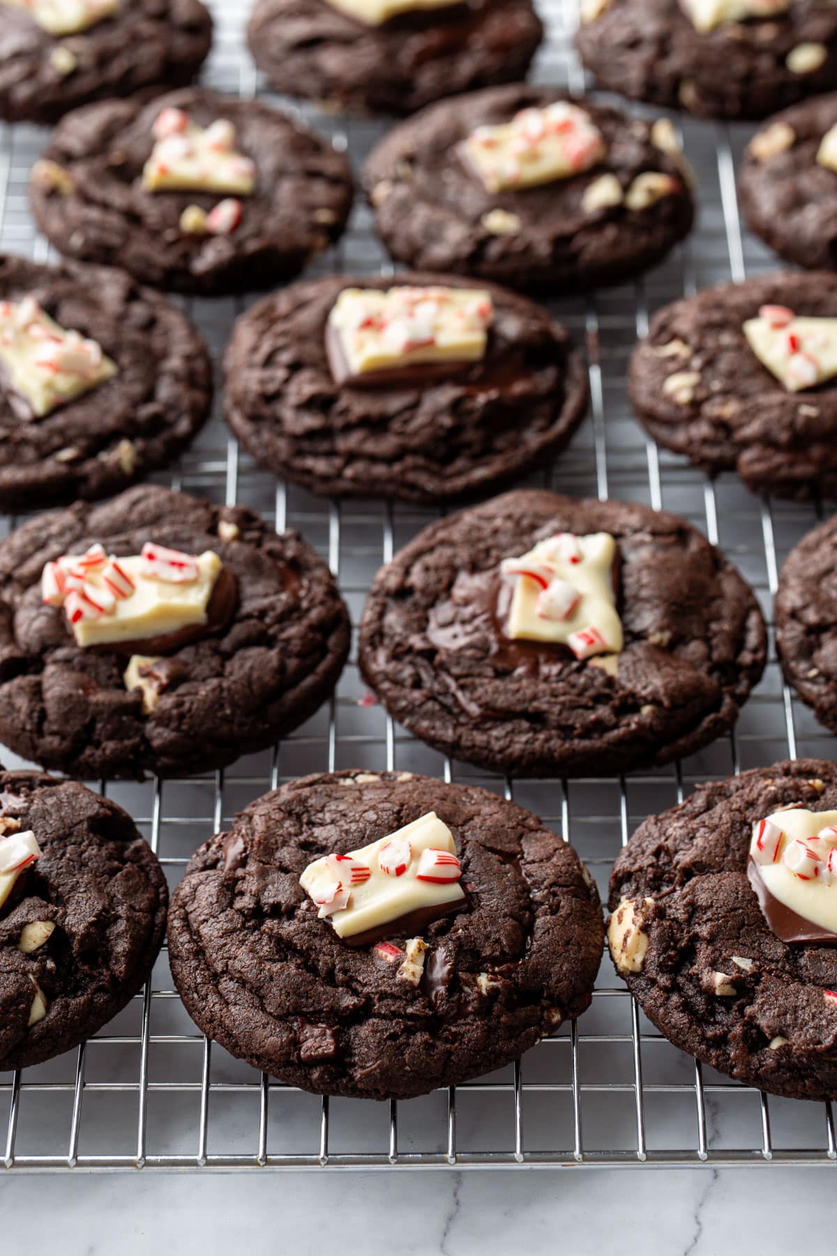 Wire rack with neat rows of cooling Chocolate Peppermint Bark Cookies, each topped with a chunk of peppermint bark.
