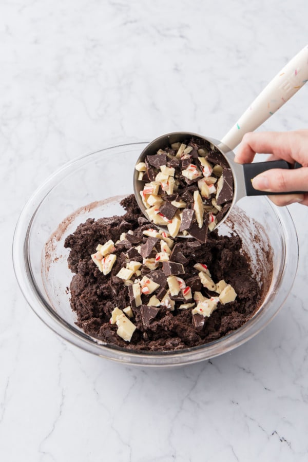 Adding chopped peppermint bark pieces to mixed cookie dough.
