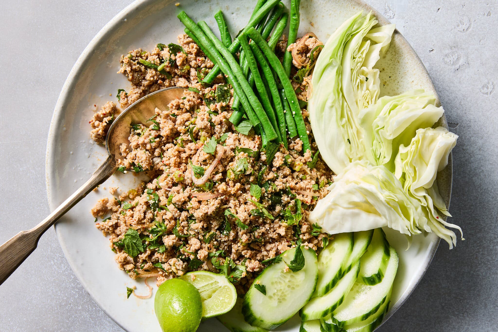 An overhead image of larb paired with green beans, cabbage and cucumbers.