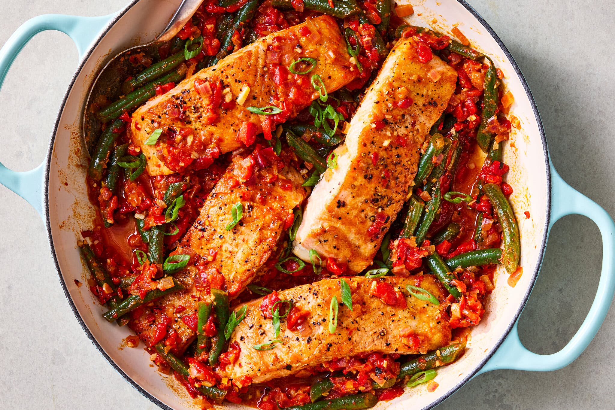 An overhead image of a Dutch oven filled with salmon, green beans and red peppers.