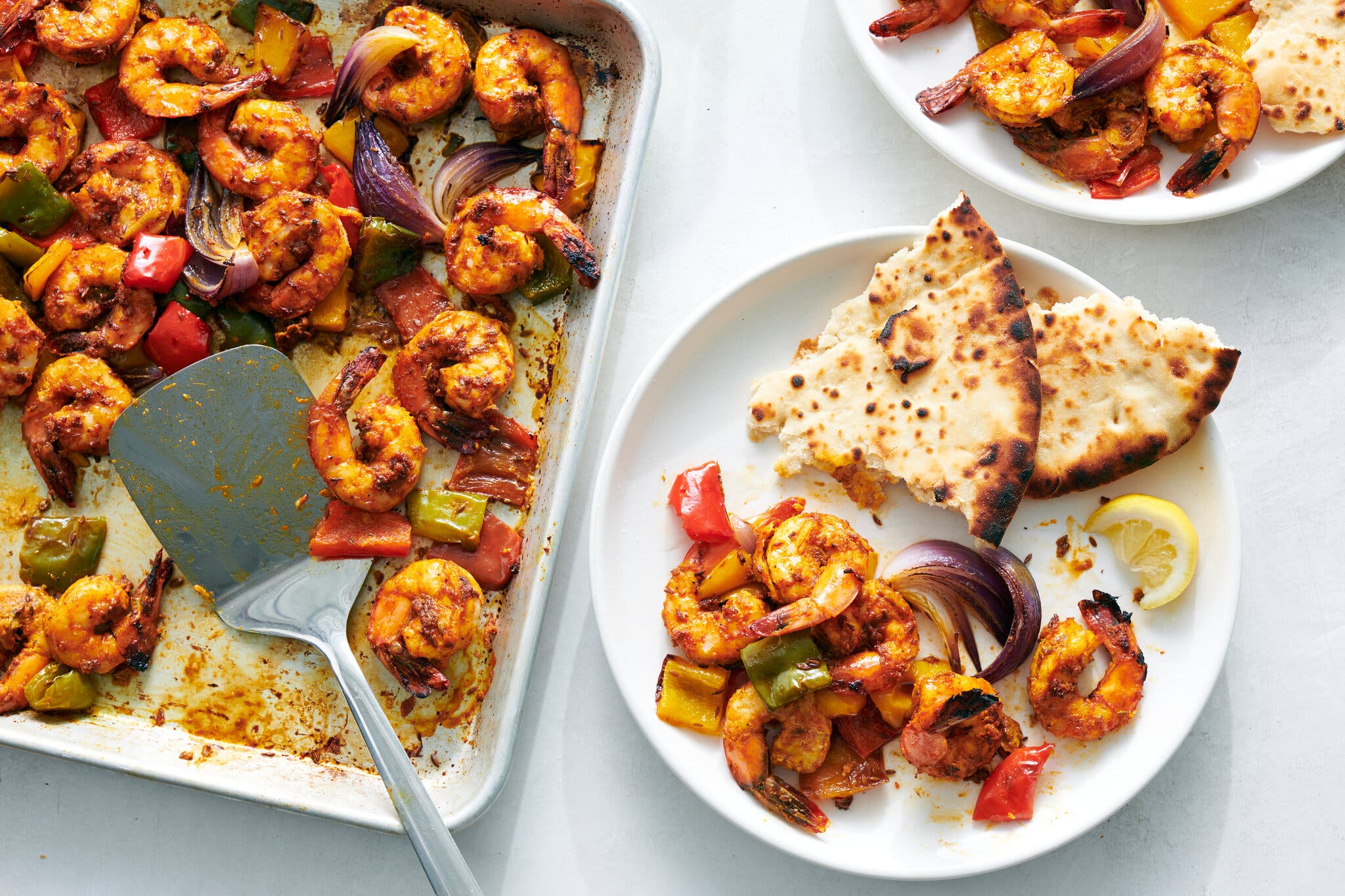 An overhead image of a sheet pan topped with shrimp and roasted onions next to a couple of servings of the dish, paired with flatbread.