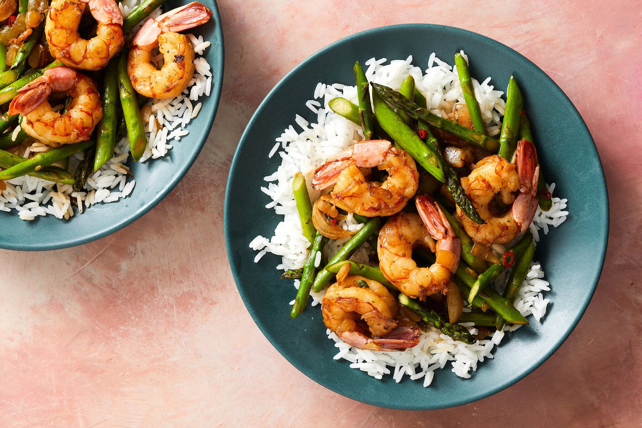An overhead image of two blue bowls topped with white rice, shrimp and asparagus.